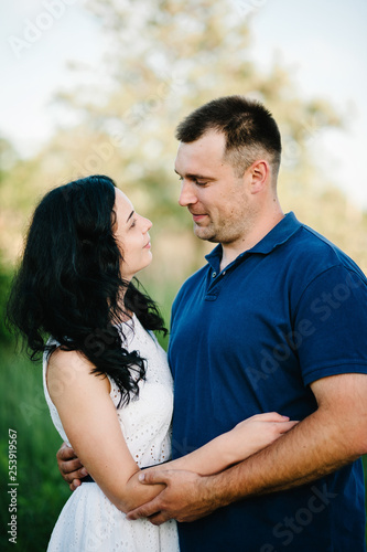 Outdoor shot of young happy couple in love standing on grass in field. Man and woman in sunlight summer park. Happy family in the evening sun light. The concept holiday. © Serhii