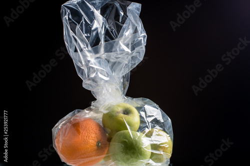 Green apples and orange in a transparent packaging bag