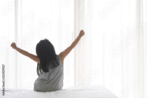 Asian child cute relax or kid girl wake up or woke up with stretch oneself after sleep for refreshing in morning on white bed and window with curtain in bedroom at home or hotel and resort on holiday