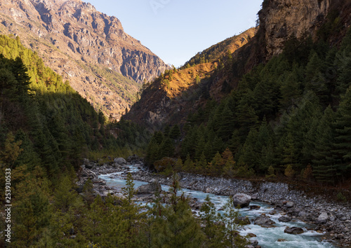 View of a river in a valley in Nepal between mountains and inside a forest. Classic view while trekking Everest Base Camp hike. 