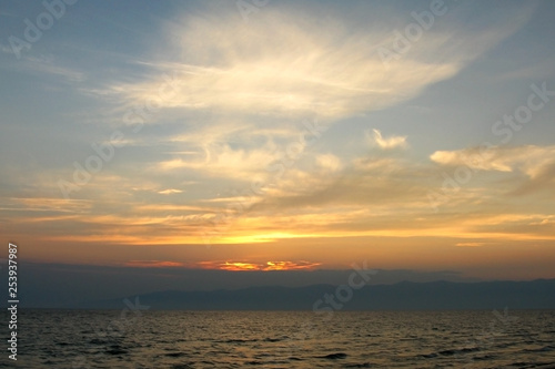Cirrus clouds in the evening sky over water, the silhouette of the mountains on the horizon, the sun goes down. Nobody. © Евгения Смирнова