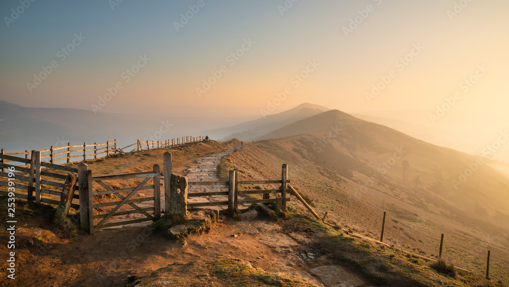 Stunning Winter sunrise landscape image of The Great Ridge in the Peak District in England with a cloud inversion and mist in the Hope Valley with a lovely orange glow