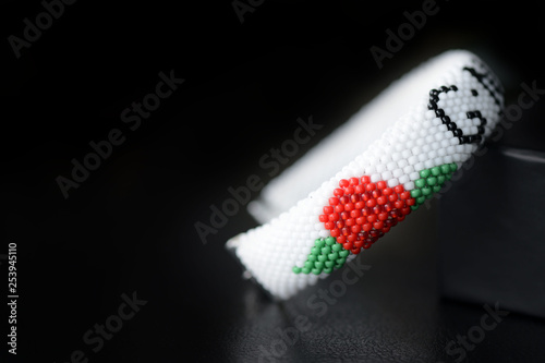White beaded bracelet with red roses on a dark background close up