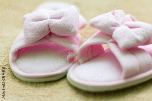 pink soft Slippers with a bow stand on a beige rug