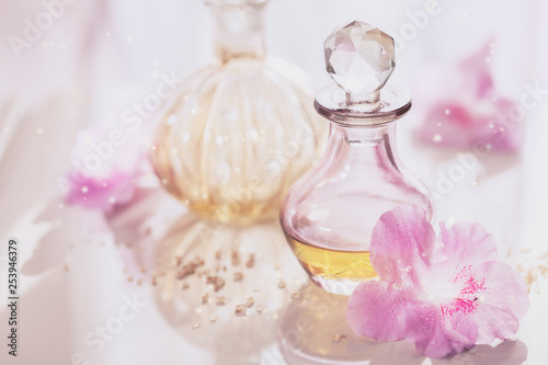Spa still life with perfume and aromatic oils bottles surrounded by flowers, on light background