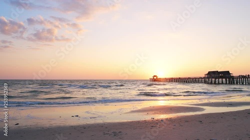 Naples, USA - April 29, 2018: Florida yellow pink purple sunset in gulf of Mexico, panning wide angle with pier wooden jetty and dead fish and sand shore photo
