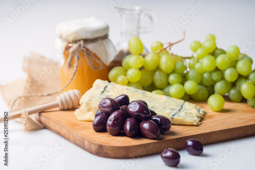 White cheese plate with olives, honey, grapes. Assortment of wine snack, appetizer or gourmet dinner. Top view