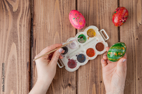 Close-up of woman's hands painting an easter egg on wooden background