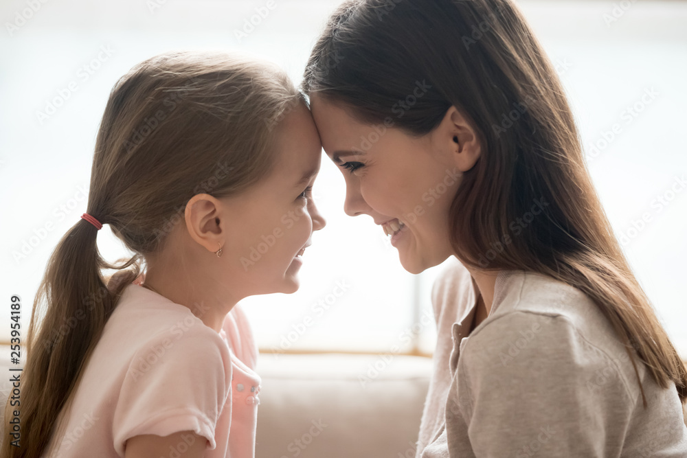 Happy kid girl and smiling mother touching foreheads, side view Happy kid girl and smiling mother touching foreheads, side view