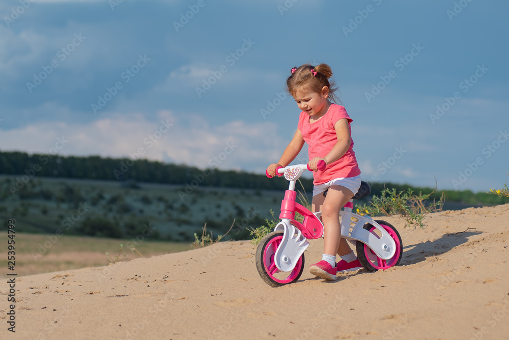 Baby sport. Overcoming difficulties and new routes. Baby girl riding on pink bicycle in the city park for children. Baby sport. Overcoming difficulties and new routes. Baby girl riding on pink bicycle in the city park for children.