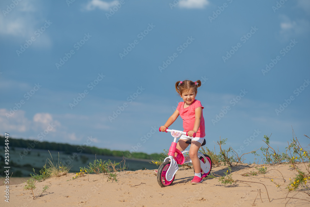 Hello spring, laughter and joy. Baby sport. Overcoming difficulties and new routes. Baby girl riding on pink bicycle in the city park for children.
