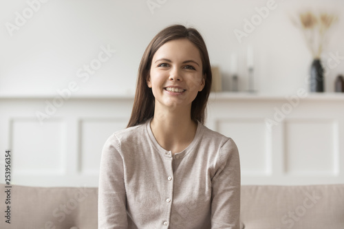 Smiling young casual woman sitting on couch looking at camera