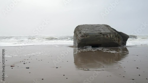 Zoom in shoot of a ruin of a bunker on the westcoat of denmark on a foggy, wet and cold wintersday with big waves hitting the beach. A relic from the Atlantic wall Hitler had built during WW2. photo