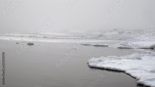 Foam and waves being washed up on the shore of the beach on a cold and foggy wintersday. photo