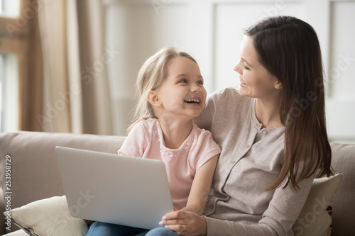 Happy mom and kid daughter laughing having fun with laptop