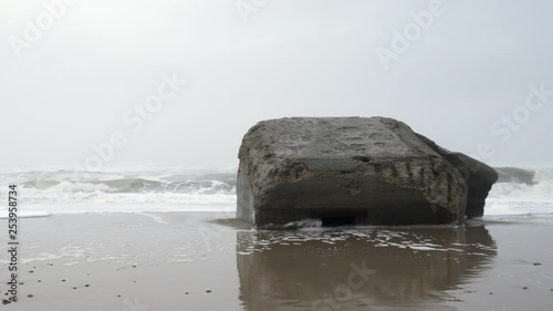 Pan left shoot of a ruin of a bunker on the westcoat of denmark on a foggy, wet and cold wintersday with big waves hitting the beach. A relic from the Atlantic wall Hitler had built during WW2. photo