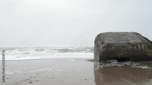 Pan right shoot of a ruin of a bunker on the westcoat of denmark on a foggy, wet and cold wintersday with big waves hitting the beach. A relic from the Atlantic wall Hitler had built during WW2. photo