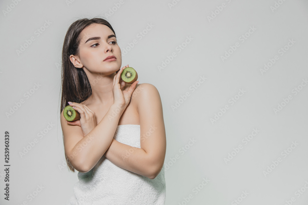 Young pretty girl standing on a white background. During this time, he put his hands crosswise and holds the kiwi halves at the level of the chest. Looking to the side. Young pretty girl standing on a white background. During this time, he put his hands crosswise and holds the kiwi halves at the level of the chest. Looking to the side.
