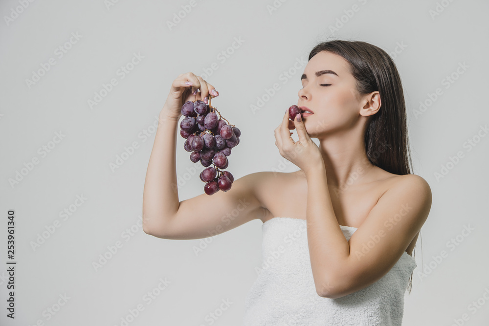 Beautiful young brunette girl with a happy smile. Holding a bunch of fresh grapes in hand, isolated on a white background.