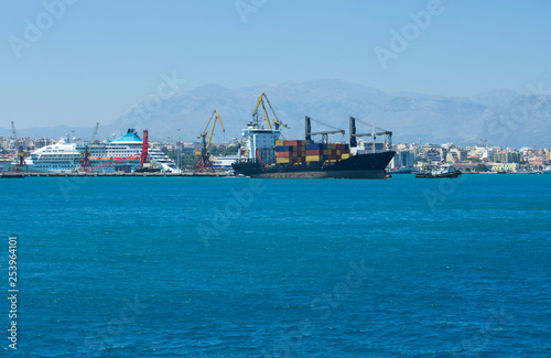 Container ship stands at the pier in the Bay of Heraklion in the background mountains and blue sky