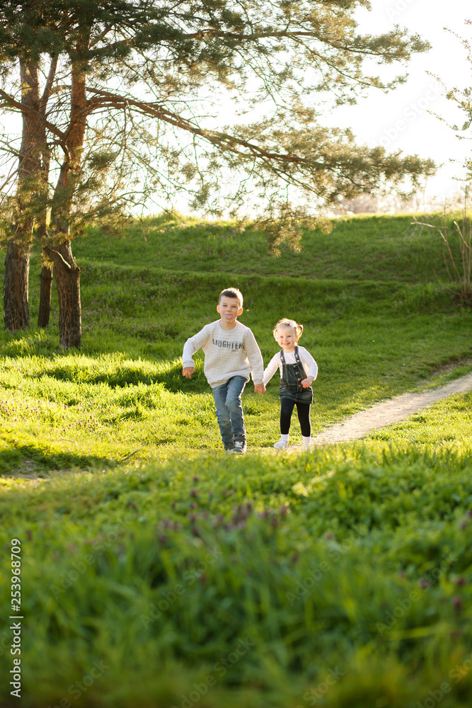 Cute children boy and girl friends running through the park in spring on a sunny day. Cute children boy and girl friends running through the park in spring on a sunny day.