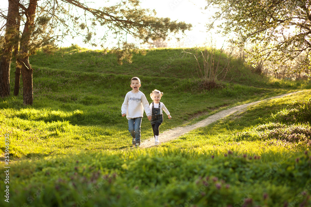 Cute children boy and girl friends running through the park in spring on a sunny day. Cute children boy and girl friends running through the park in spring on a sunny day.