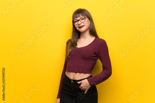 Woman with glasses over yellow wall laughing looking to the front