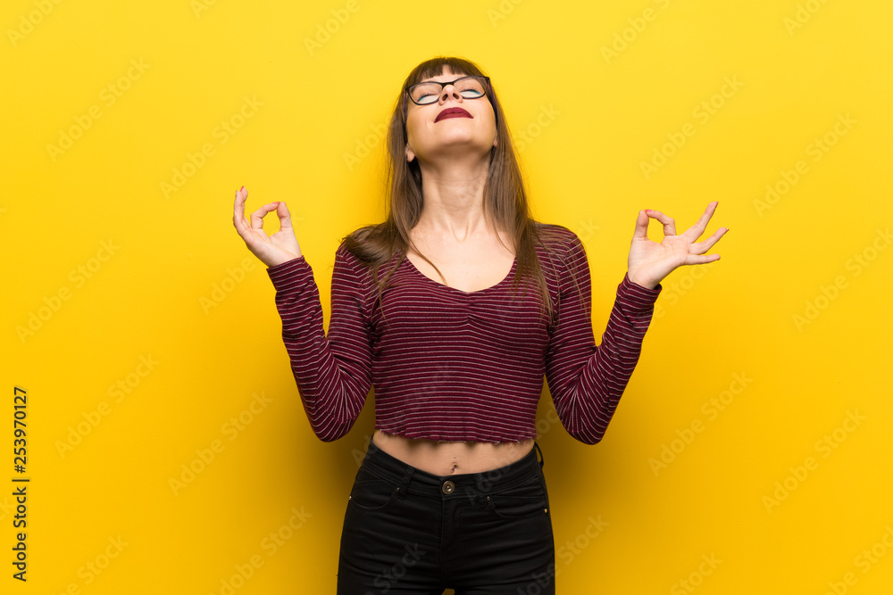 Woman with glasses over yellow wall in zen pose Woman with glasses over yellow wall in zen pose