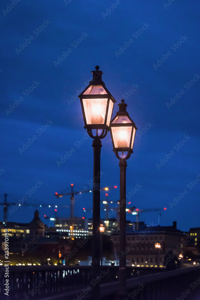 Illuminated street lanterns at night and construction site cranes in the background, Stockholm, Sweden