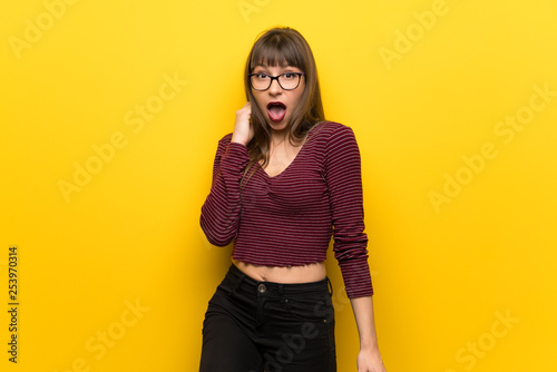 Woman with glasses over yellow wall with surprise and shocked facial expression
