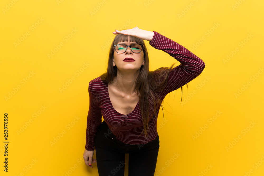 Woman with glasses over yellow wall looking far away with hand to look something Woman with glasses over yellow wall looking far away with hand to look something
