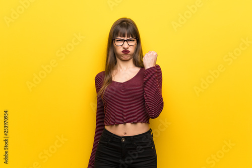 Woman with glasses over yellow wall with angry gesture