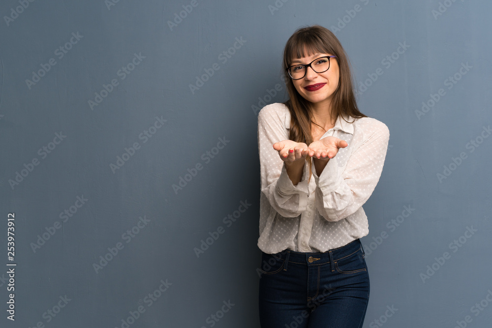 Woman with glasses over blue wall holding copyspace imaginary on the palm to insert an ad Woman with glasses over blue wall holding copyspace imaginary on the palm to insert an ad