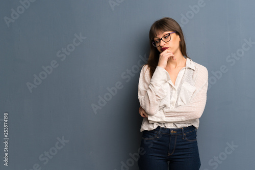 Woman with glasses over blue wall having doubts