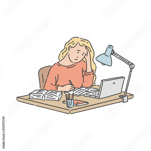 Stressed student girl sitting at table with laptop and notebook and studying.