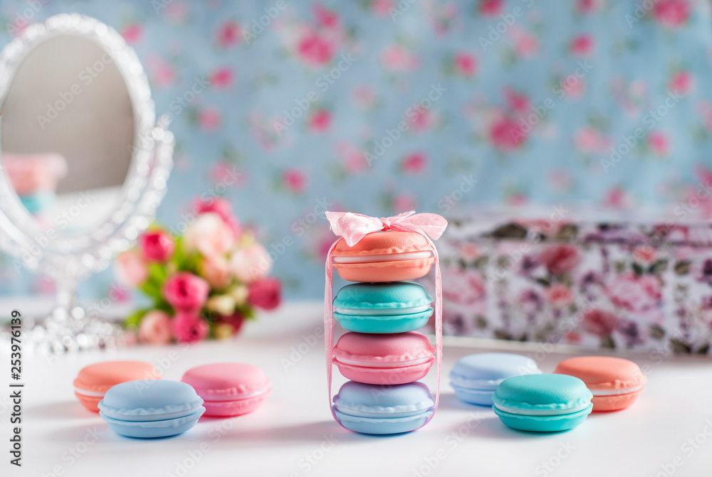 Spring design in delicate pastel colors with macaroons, a bouquet of roses, a mirror and a casket on a white table on a floral background Spring design in delicate pastel colors with macaroons, a bouquet of roses, a mirror and a casket on a white table on a floral background