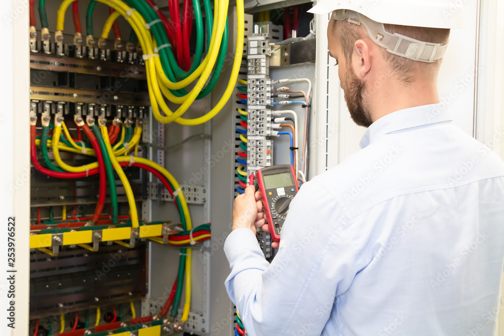 Electrician engineer with measuring tool works in electrical cabinet