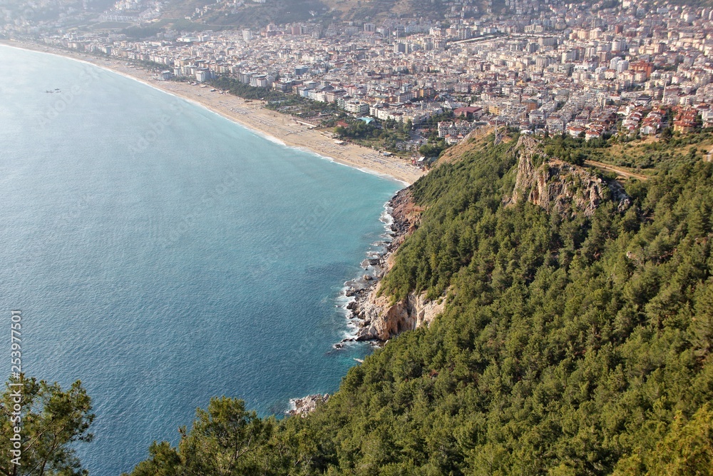 View from the fortress in the foreground part of the mountain with the forest and in the background Cleopatra's beach and the city of Alanya on a blurred background