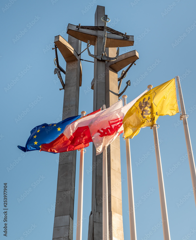 Monument to the fallen workers of shipyard at Solidarnosc Square in Gdansk with flags in front.