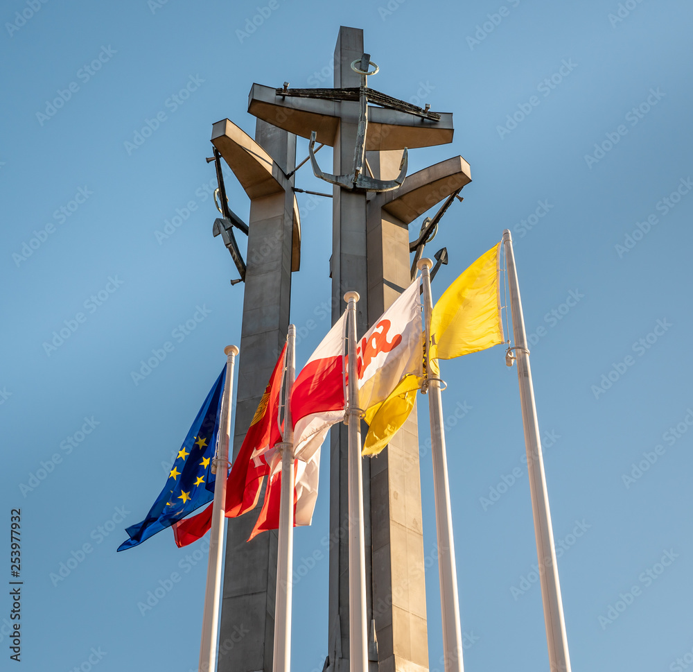 Monument to the fallen workers of shipyard at Solidarnosc Square in Gdansk with flags in front.