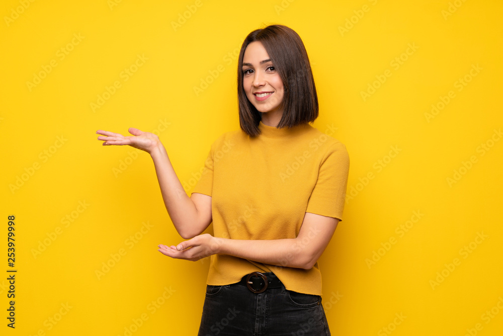 Young woman over yellow wall extending hands to the side for inviting to come Young woman over yellow wall extending hands to the side for inviting to come
