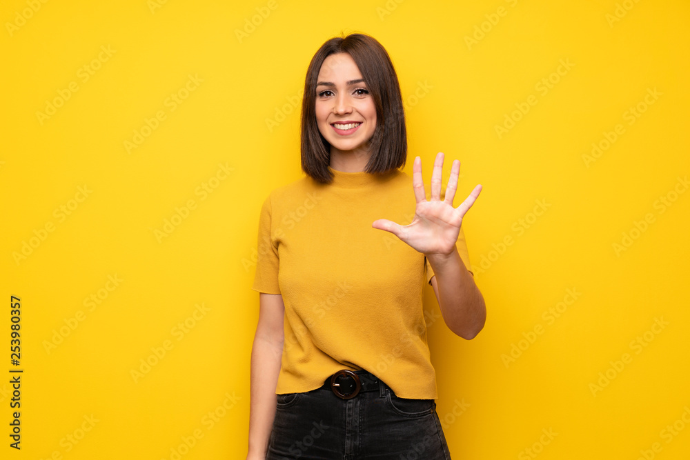 Young woman over yellow wall counting five with fingers Young woman over yellow wall counting five with fingers