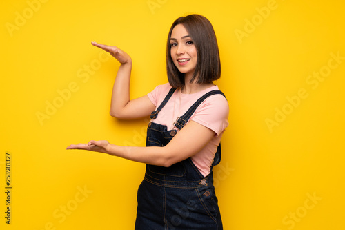 Young woman over yellow wall holding copyspace to insert an ad