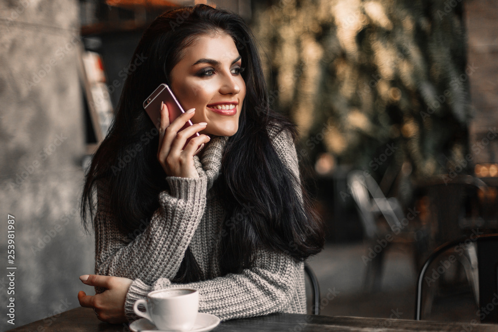 Woman using phone and drinking coffee in a cafe.