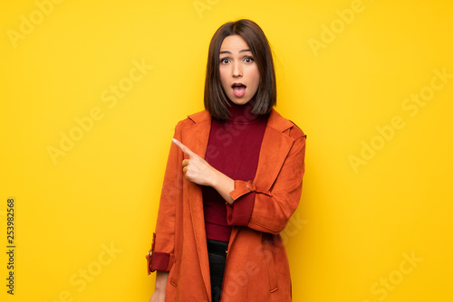 Young woman with coat surprised and pointing finger to the side © luismolinero
