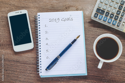 2019 goals text on book note with cup of coffee, pen and smartphone.