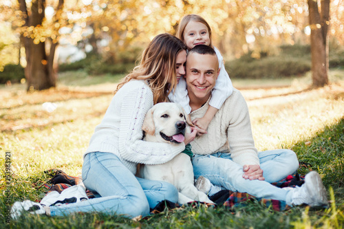 Happy beautiful family with dog labrador is having fun  are sitting on green grass in park.