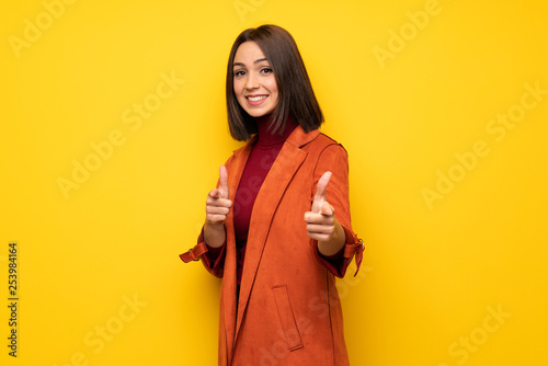Young woman with coat pointing to the front and smiling © luismolinero