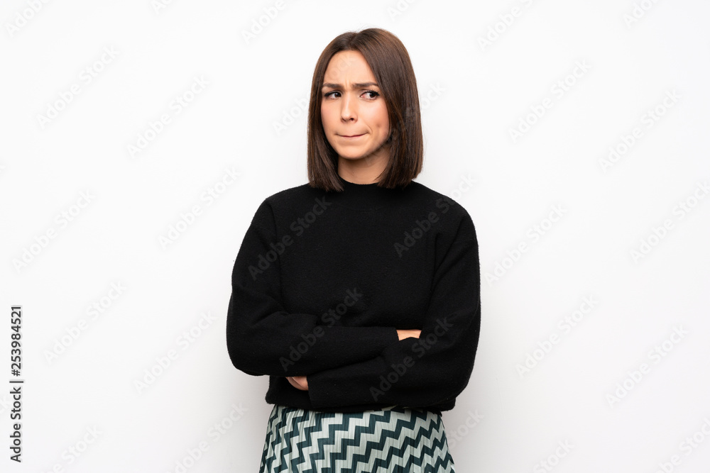 Young woman over white wall with confuse face expression while bites lip Young woman over white wall with confuse face expression while bites lip