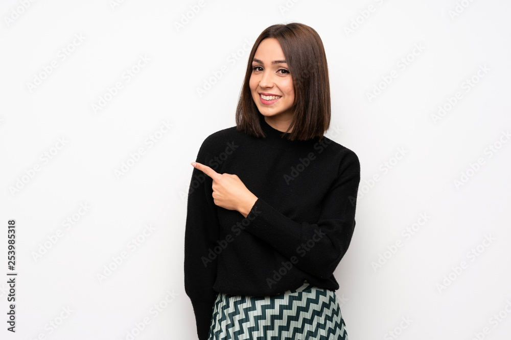 Young woman over white wall pointing to the side to present a product Young woman over white wall pointing to the side to present a product